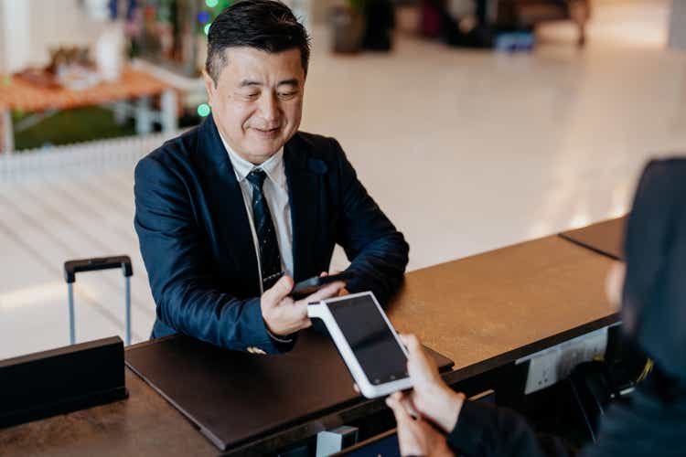 Senior businessman using smartphone for contactless payment at hotel reception