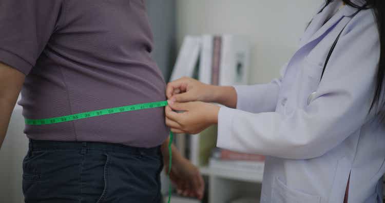 Female Nutritionist measuring waist of overweight man in weight loss clinic