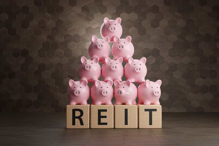 Heap of pink piggy banks on wooden blocks written with the alphabet REIT. Illustration of the concept of real estate investment trust