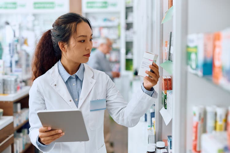 Female Chinese pharmacist using digital tablet while working in a pharmacy.