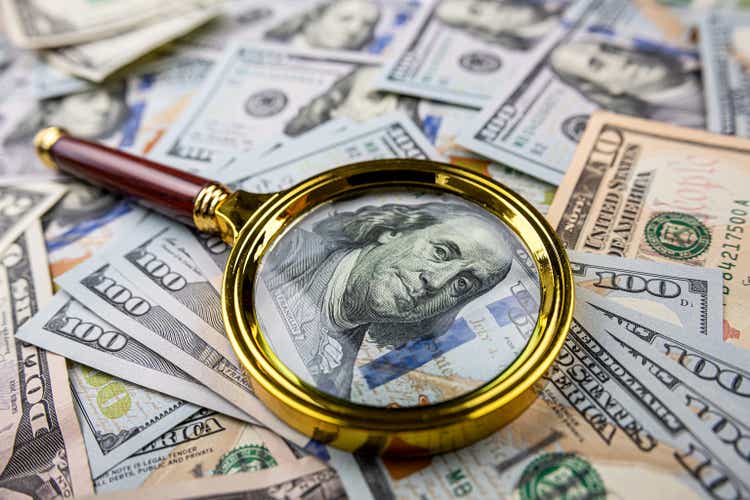 Golen magnifying glass on different dollars money as financial background
