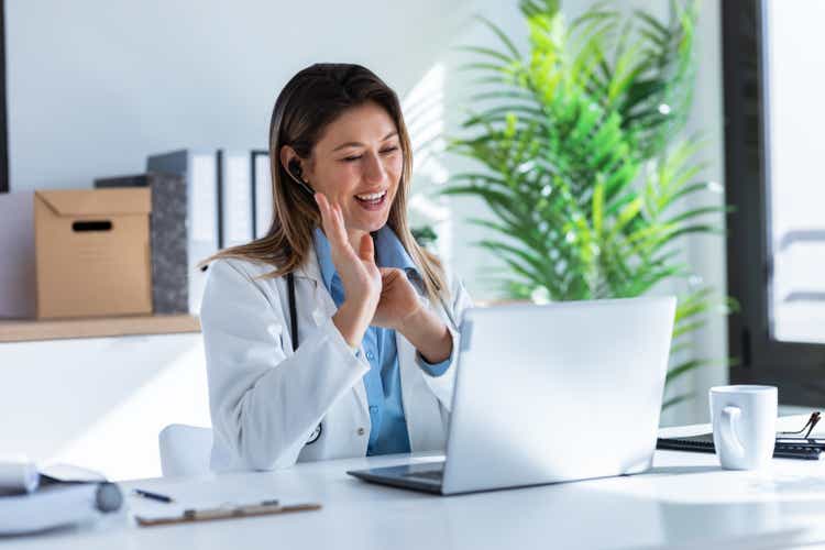 Female doctor talking with colleagues through a video call with a laptop in the consultation.