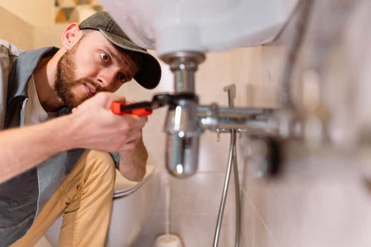 A plumber is carefully fixing a leaking sink with a wrench