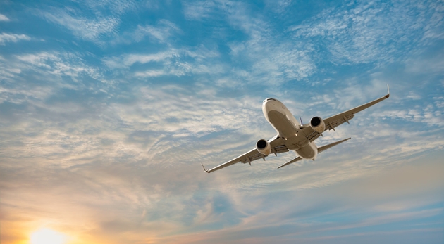 Airplane flying over tropical sea at sunset