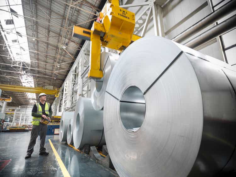 Worker operating crane with steel rolls in car factory