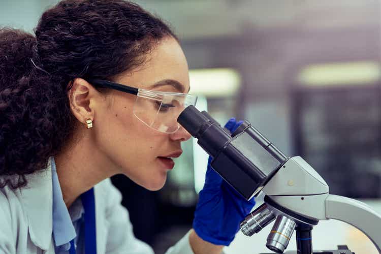 Close-up of female scientist looking through microscope at work desk