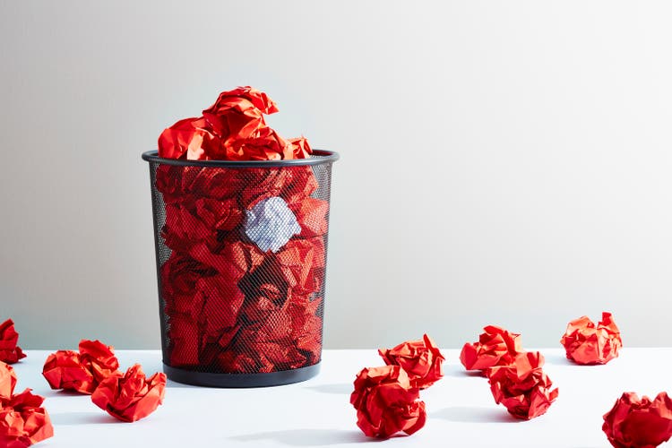 A waste paper basket full of red crumpled paper