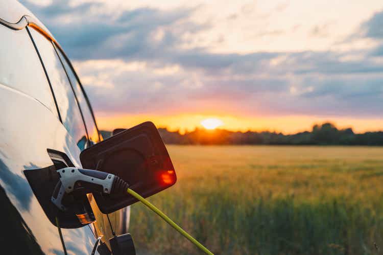 An electric car plugged in against a background of a rural location at sunset