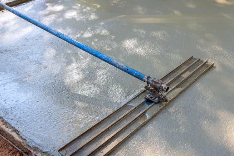 The concrete for driveway is being leveled by workers on construction site using mix concrete trowels