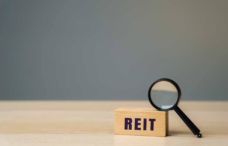 Reit inscription on a wooden block. Real estate investment trust concept. Company that owns, operates, or finances income-generating real estate. Magnifying glass