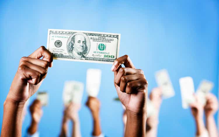 Hands hold up US $100 bill with more in background
