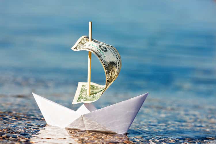 Paper boat with $1 bill sail is blown onshore