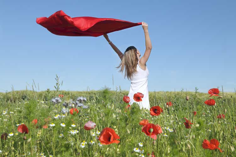 Woman Standing in Poppy Field Holding red scarf to Wind