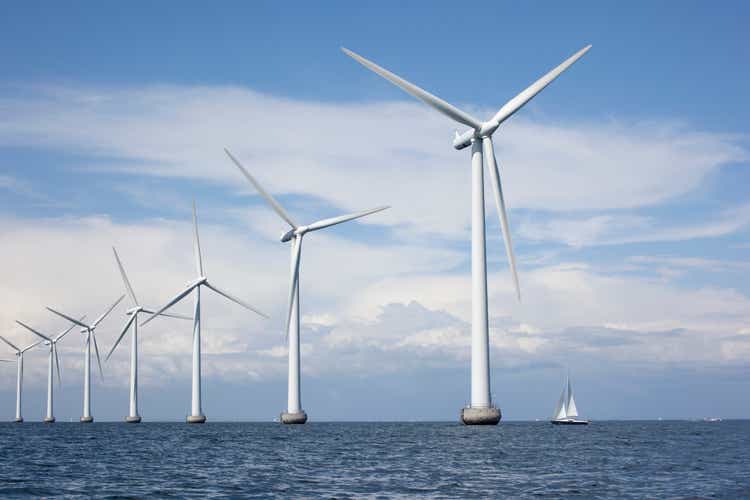 Large white windmills in the sea with a sailboat
