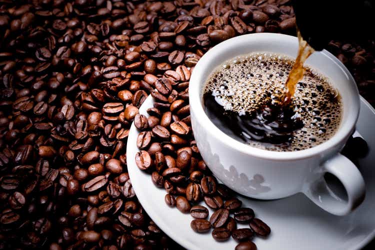 Mug on plate filled with coffee surrounded by coffee beans 