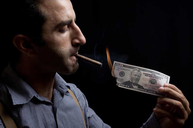 Adult man lighting up a cigar with burnt dollar bill