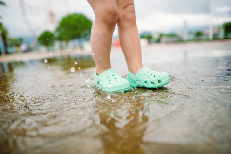 Little girl playing with puddles and splashing water in a park in summer after rain