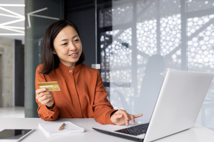 Young successful businesswoman smiling and looking at laptop, Asian woman holding bank credit card and shopping online in online store, woman with laptop at workplace
