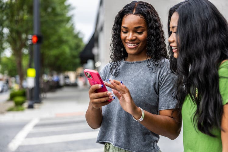 Two young women walking down urban street and using smartphone