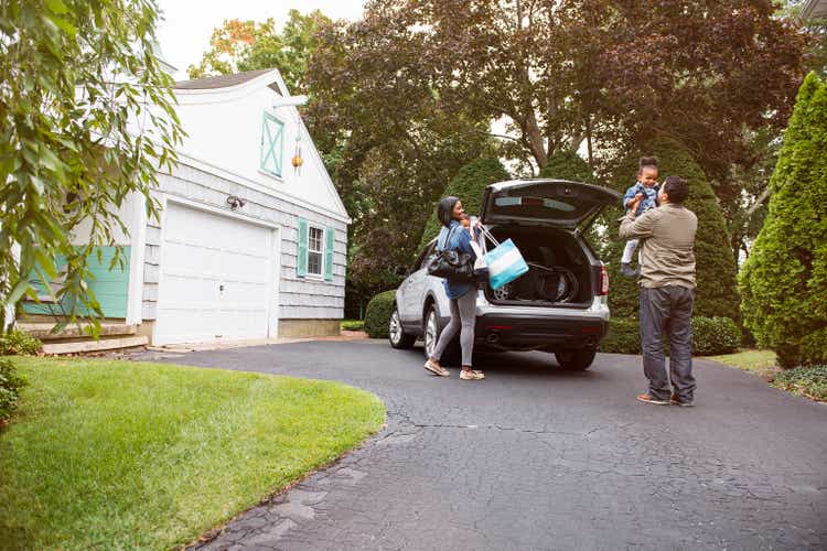 Family standing by car on driveway outside house