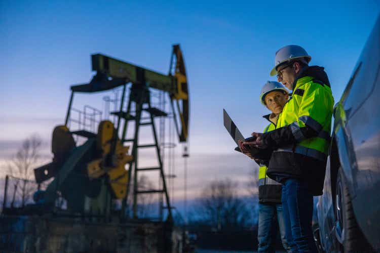 Partners planning over laptop while standing against equipment by car at field