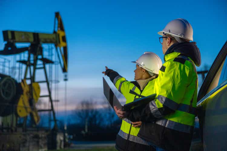 Engineers looking at machinery while planning over laptop by car at oil field