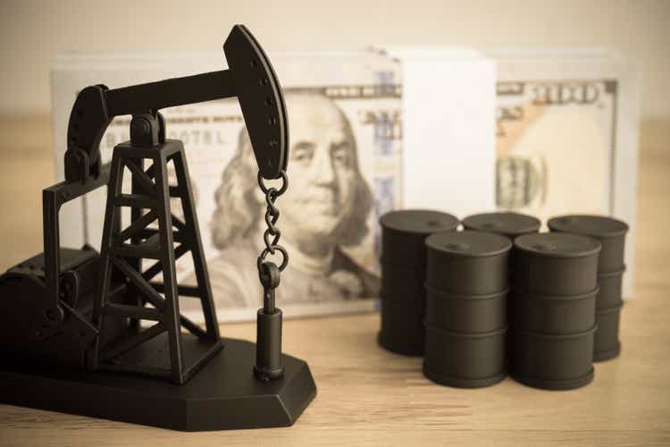 Oil pump jack, oil tank and US banknotes bill on table.