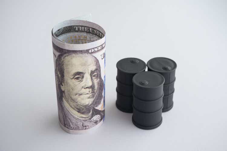 US-Dollar-Banknoten und schwarzer Rohöltank auf weißem Hintergrund.