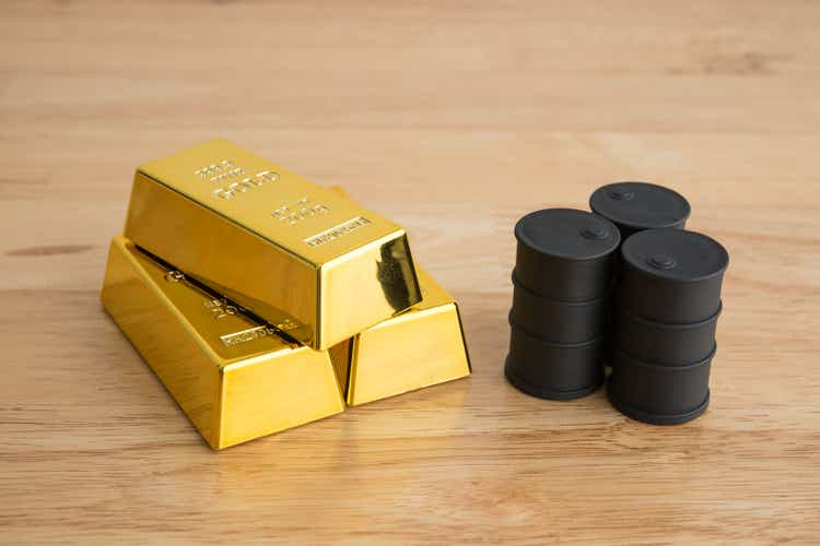 Black crude oil tanks vs gold bars on wooden background.