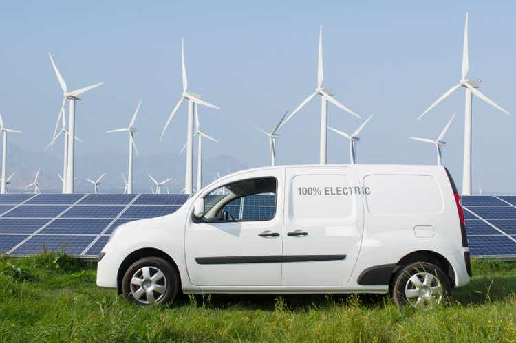 Electric van in front of solar panels and wind turbines