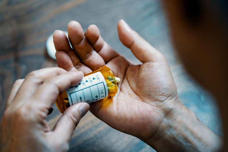 Close-up of a male hand holding a pill bottle pouring medication into his hand