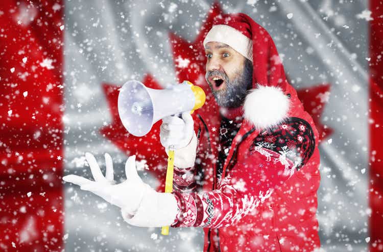 Santa Claus shouts into a megaphone and shows a hand gesture against the background of the flag of Canada