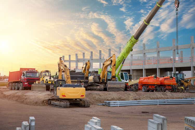 Construction site parking area with many different colorful heavy industrial machinery and equipment against warehouse building city infrastructure development.Commercial vehicle rental sales