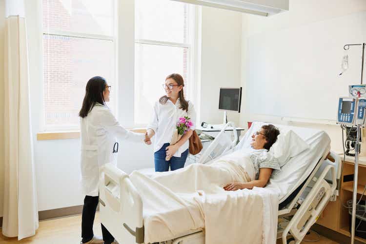 Wide shot doctor shaking hands with daughter before consulting with mother in hospital