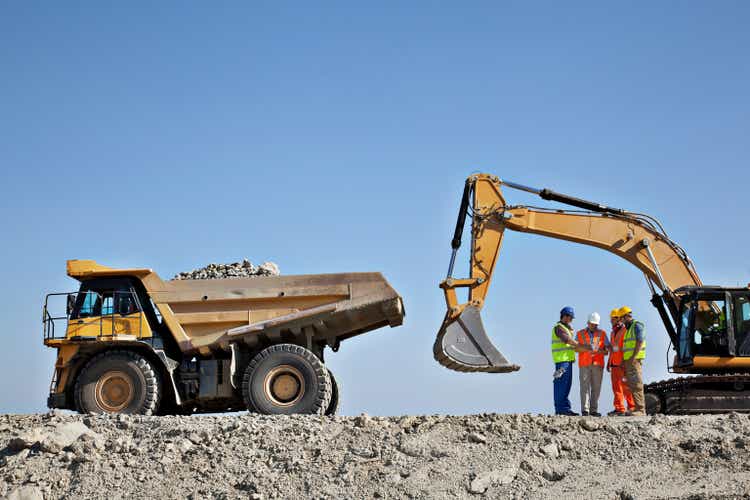 Workers talking by machinery in quarry