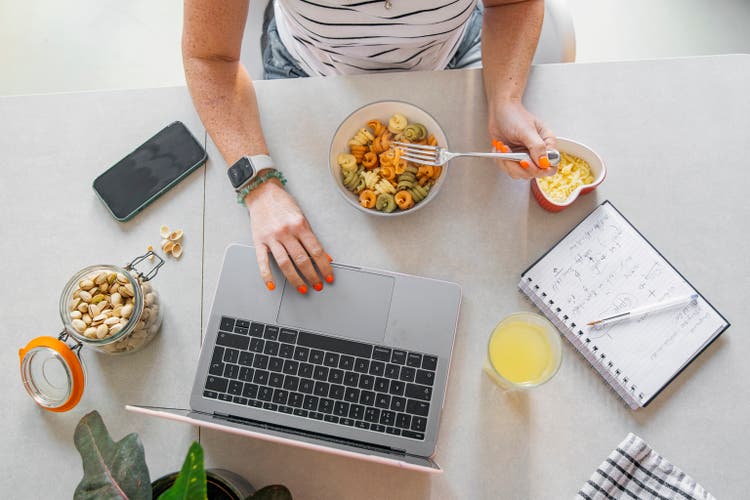 An unrecognisable woman eats a bowl of freshly cooked pasta whilst working from home