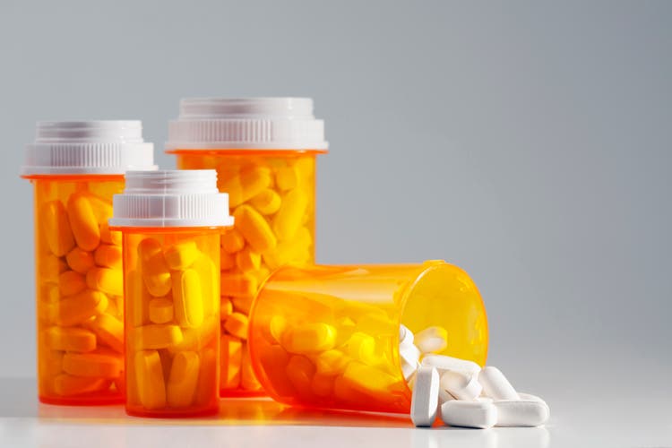 Four full prescription bottles with one spilling medication