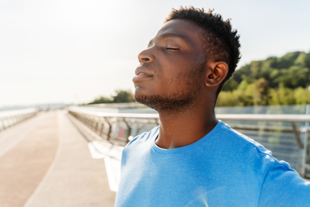 Attractive Nigerian man in blue t shirt standing on street with closed eyes, relaxing after training