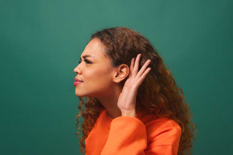 Young biracial woman cups ear, listening intently, green studio background