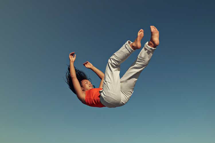 Side view of young woman falling against clear blue sky