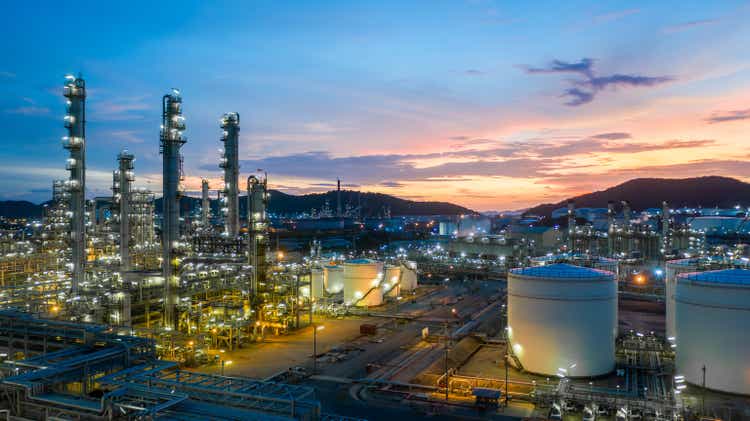 Aerial view of oil and gas tank with background of oil refinery at night, glitter lighting of petrochemical plant at night, oil production, product tank in petrochemical plant.