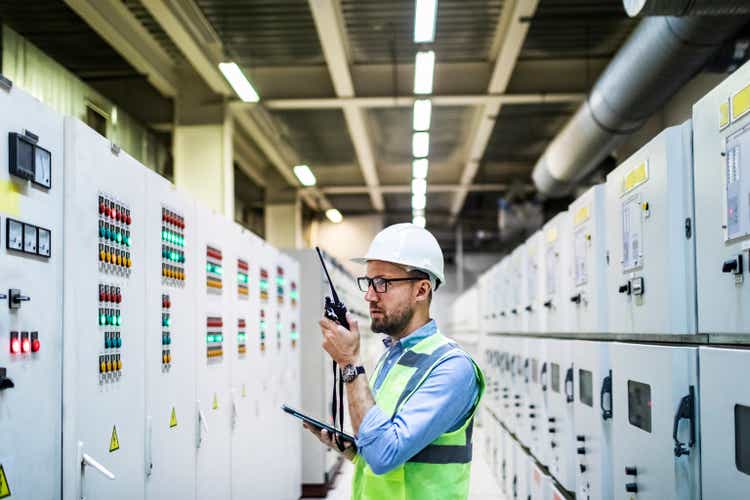 Electrical engineer checking power at control room using digital tablet and walkie-talkie