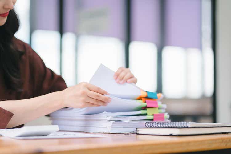 Businesswoman sifting through stacks of paper files and folders that contain both incomplete and completed documents. Selective focus