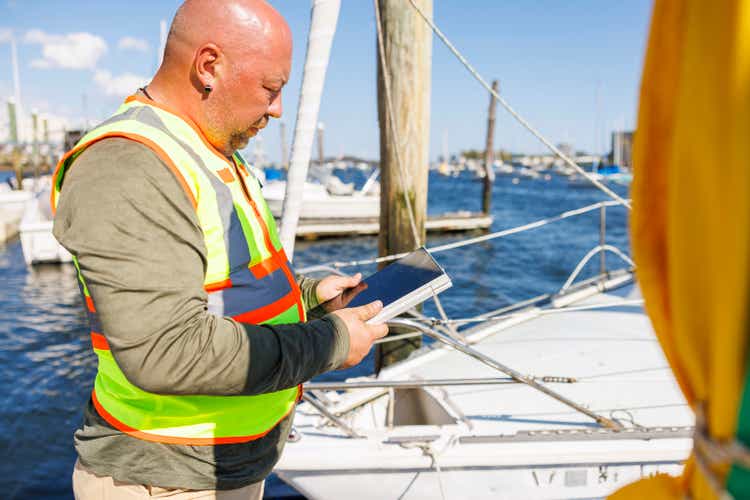 Compensation insurance of yacht damage.Claim agent with digital tab evaluating risks and insurance of yacht in pier