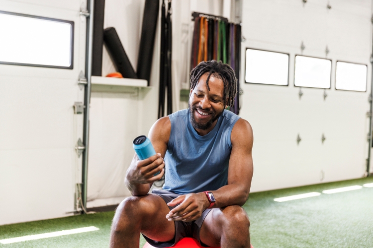 Smiling man holding energy drink while sitting at health club
