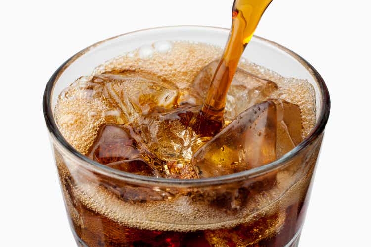 Soda being poured into glass with ice