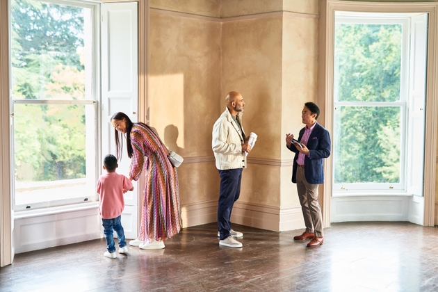 Real estate agent taking to mature man as mother and son look out of window