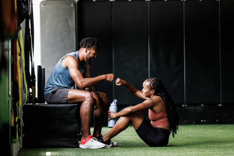 Young man giving fist bump to female friend at gym