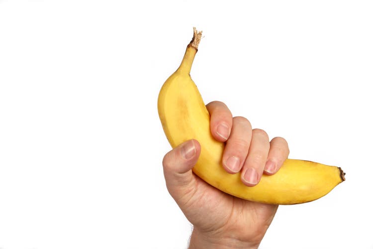 Hand holding a banana up on a white background
