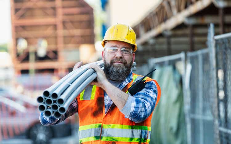 Construction worker carrying pipes on shoulder